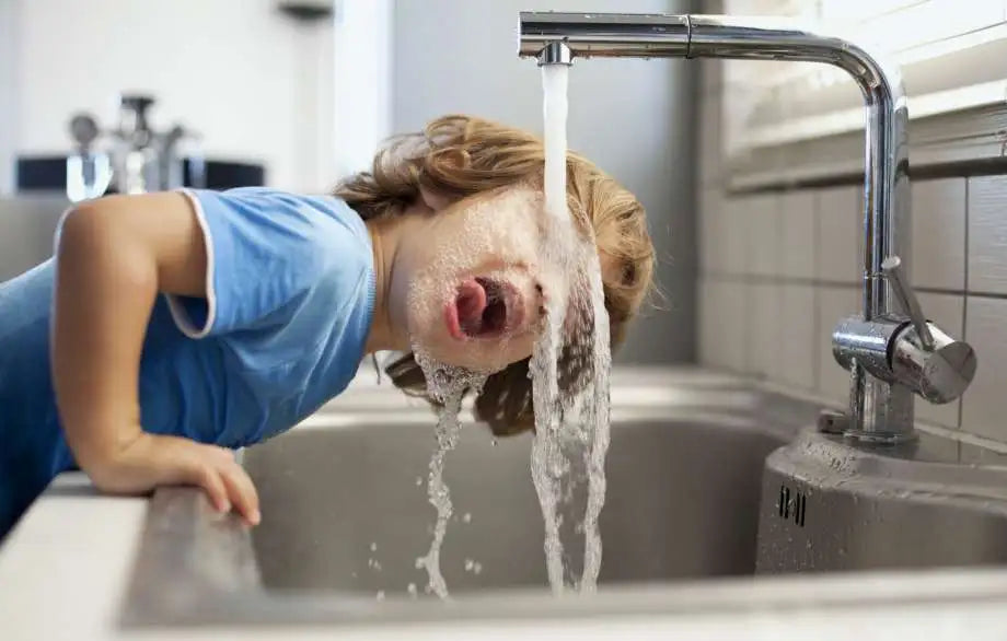 young boy drinking tap water from kitchen faucet