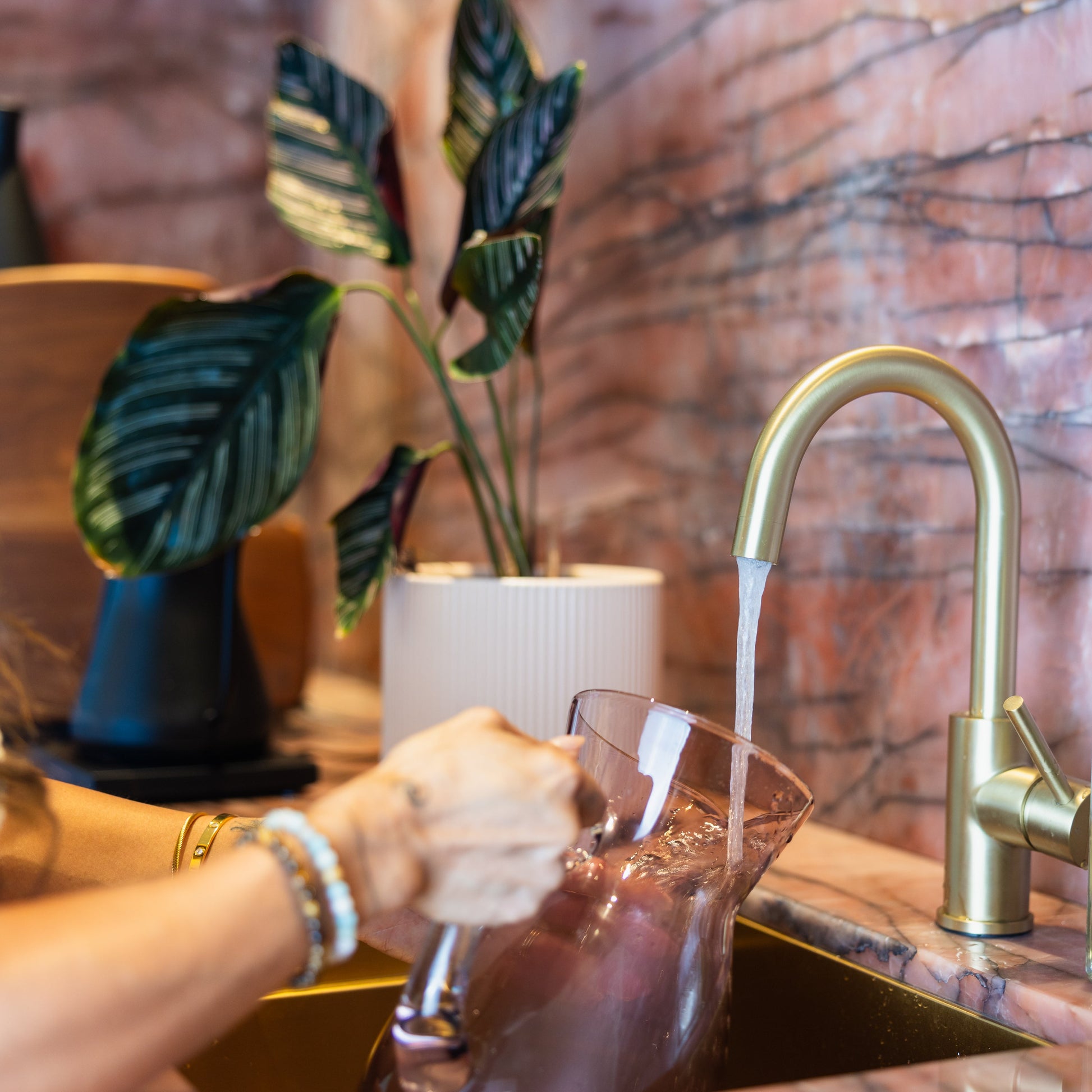 Person washing dishes in a kitchen with a gold faucet and marble backsplash.