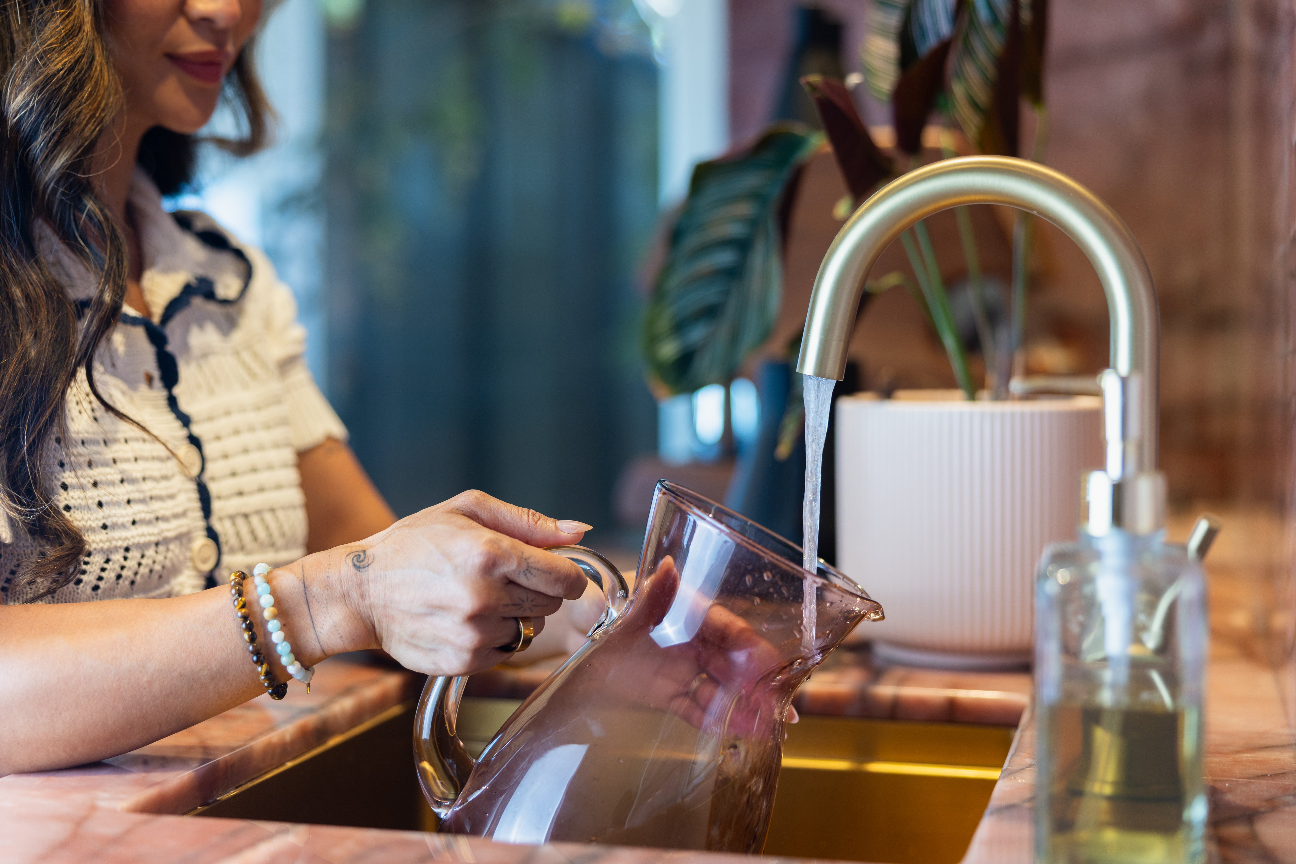 Person pouring water from a glass pitcher into a sink with a blurred background