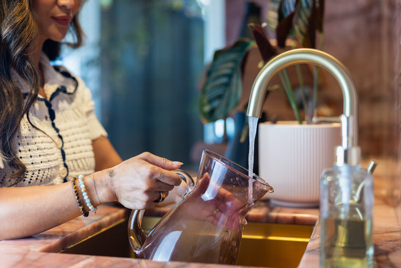 Person pouring water from a glass pitcher into a sink with a blurred background